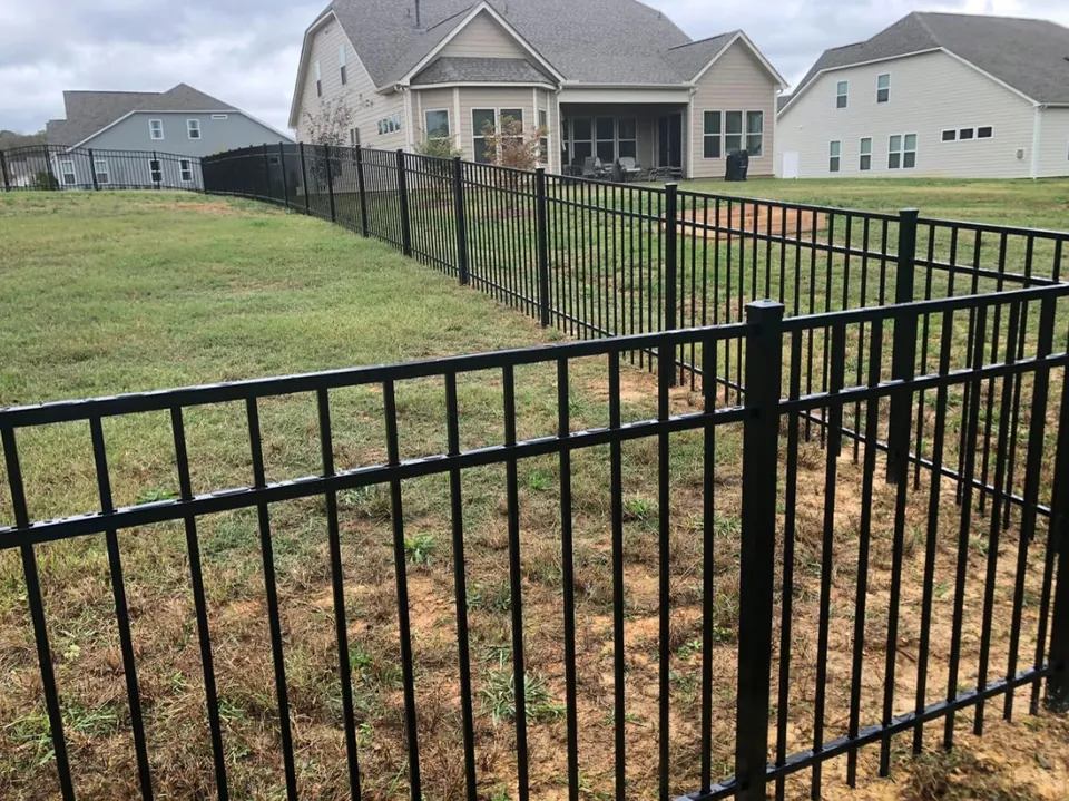 Black aluminum fence running along a suburban backyard lawn with houses behind.